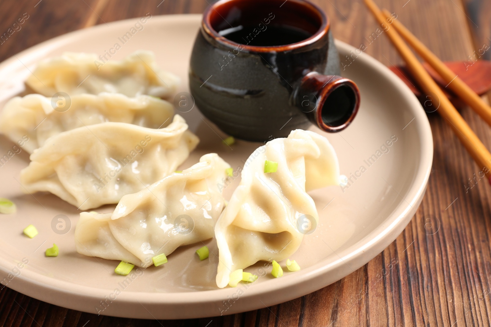 Photo of Tasty gyoza (dumpling), soy sauce and chopsticks on wooden table, closeup