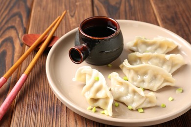 Photo of Tasty gyoza (dumpling), soy sauce and chopsticks on wooden table, closeup