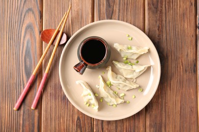 Photo of Tasty gyoza (dumpling), soy sauce and chopsticks on wooden table, top view