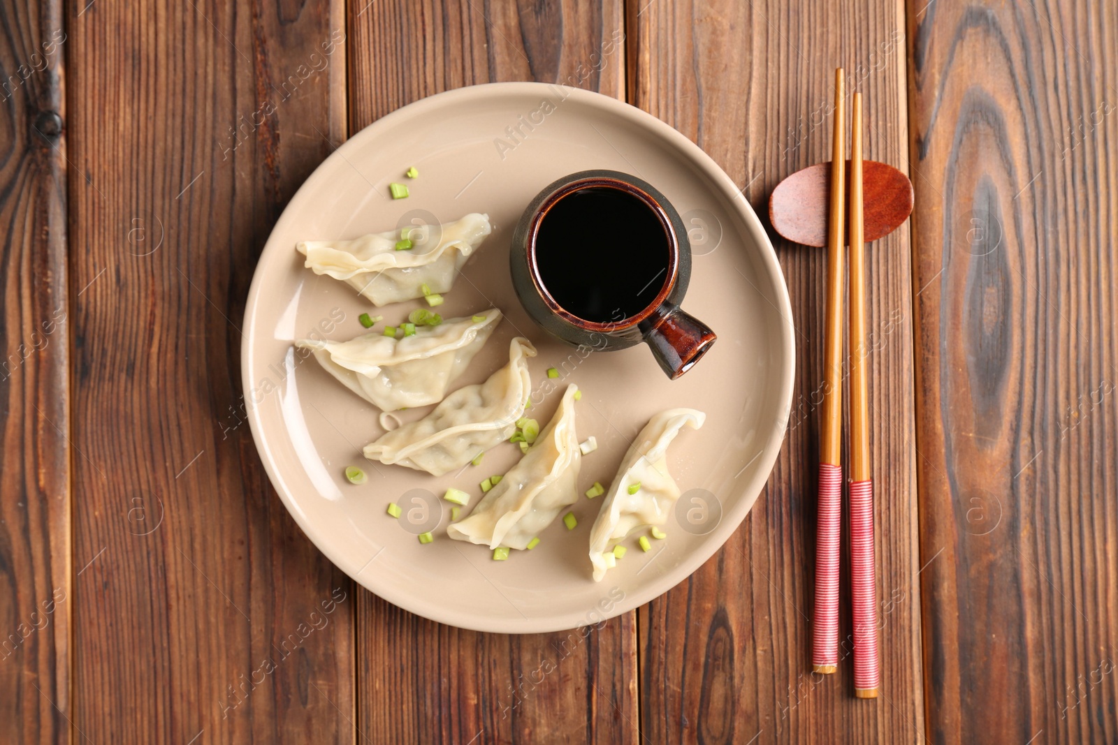 Photo of Tasty gyoza (dumpling), soy sauce and chopsticks on wooden table, top view