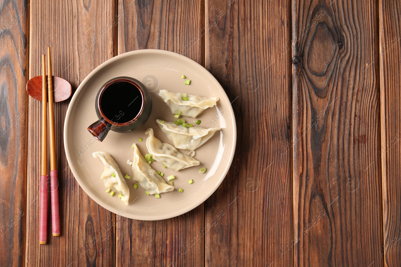 Photo of Tasty gyoza (dumpling), soy sauce and chopsticks on wooden table, top view. Space for text