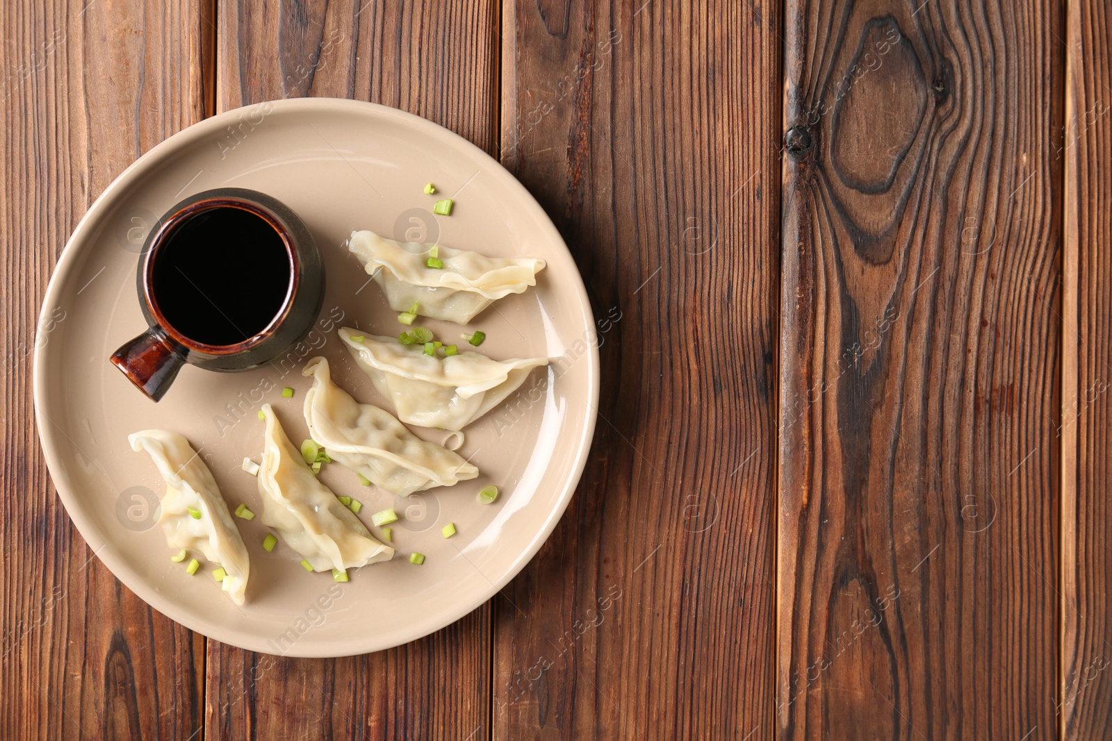 Photo of Tasty gyoza (dumplings) and soy sauce on wooden table, top view. Space for text