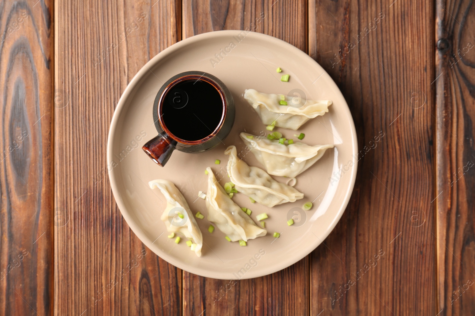 Photo of Tasty gyoza (dumplings) and soy sauce on wooden table, top view