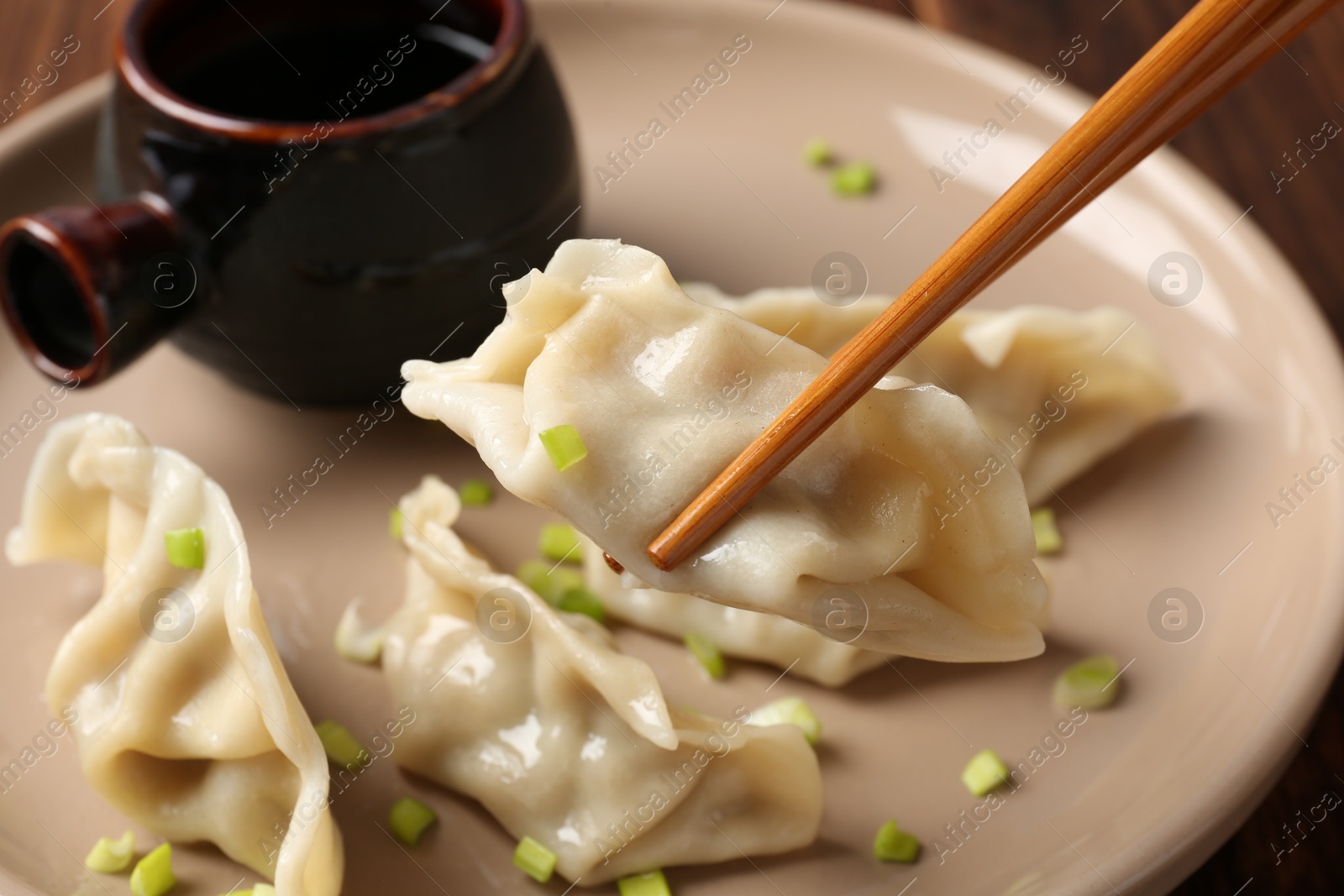 Photo of Taking tasty gyoza (dumpling) with chopsticks at table, closeup