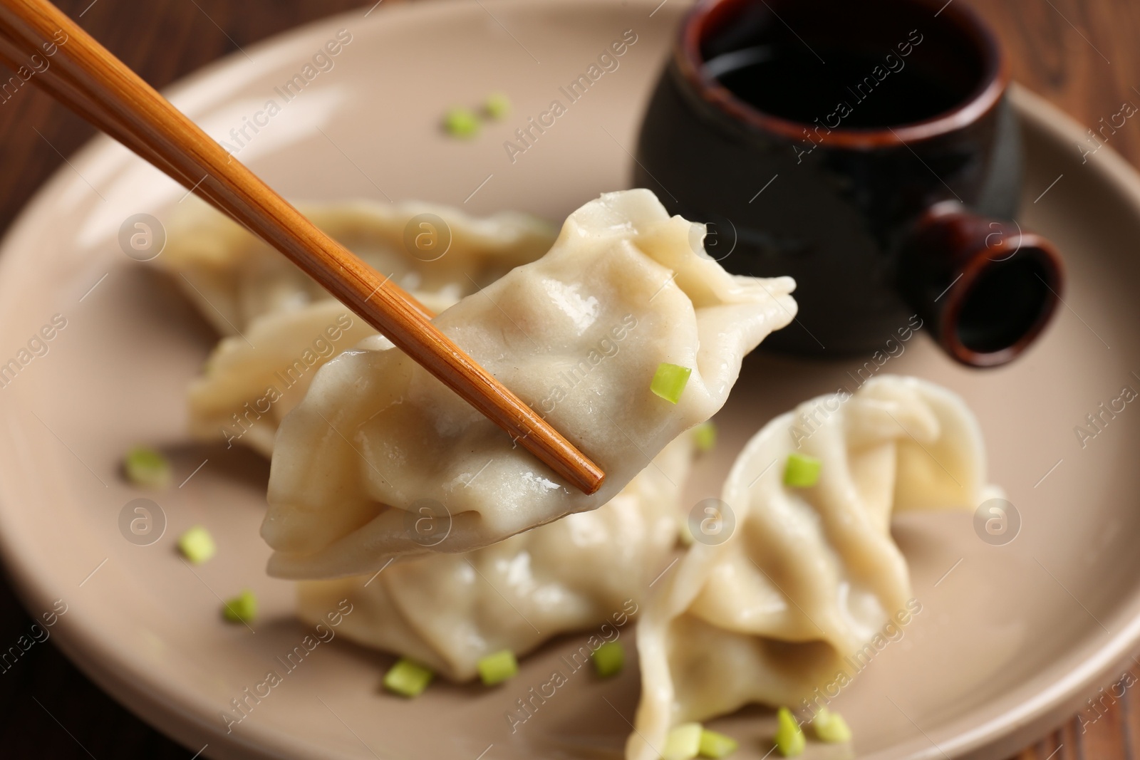 Photo of Taking tasty gyoza (dumpling) with chopsticks at table, closeup