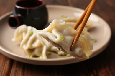 Photo of Taking tasty gyoza (dumpling) with chopsticks on wooden table, closeup