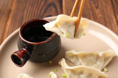 Photo of Taking tasty gyoza (dumpling) with chopsticks on wooden table, closeup