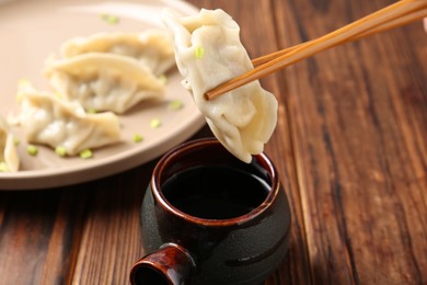 Photo of Dipping tasty gyoza (dumpling) into soy sauce at wooden table, closeup