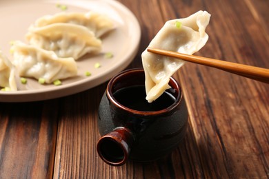 Photo of Dipping tasty gyoza (dumpling) into soy sauce at wooden table, closeup