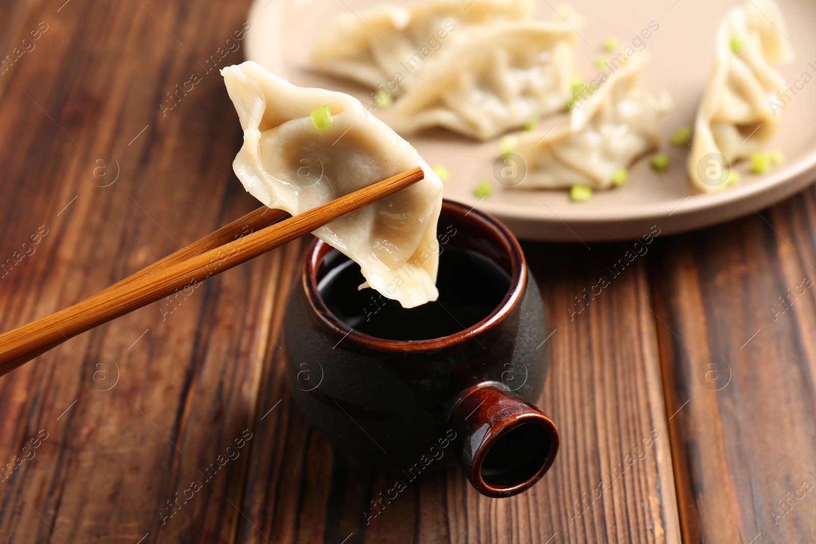 Photo of Dipping tasty gyoza (dumpling) into soy sauce at wooden table, closeup