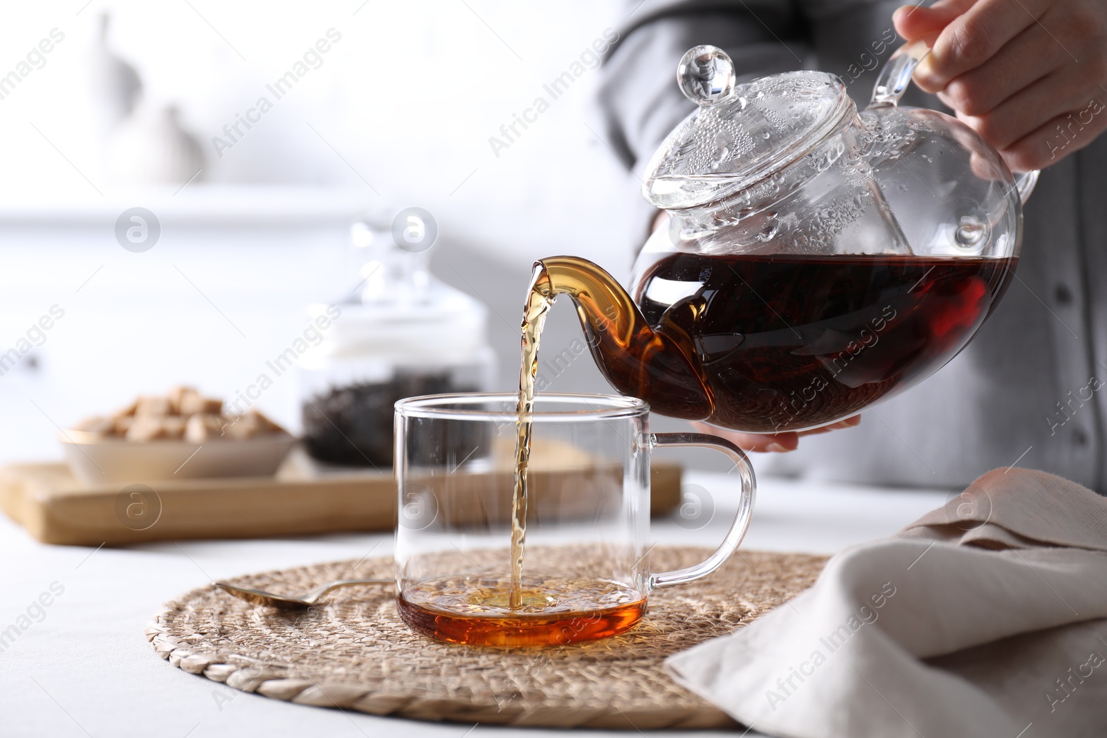 Photo of Woman pouring hot black tea into cup at white table, closeup