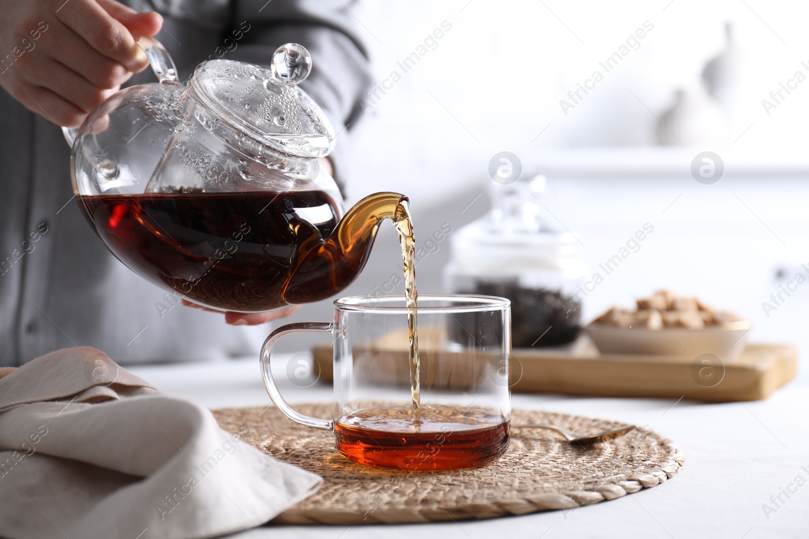 Photo of Woman pouring hot black tea into cup at white table, closeup