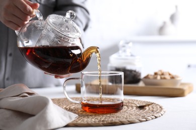 Photo of Woman pouring hot black tea into cup at white table, closeup