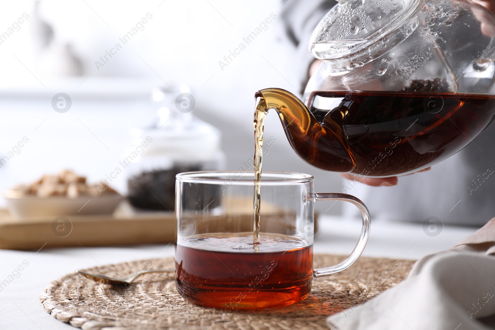 Photo of Woman pouring hot black tea into cup at white table, closeup