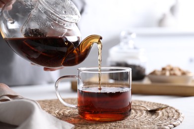 Photo of Woman pouring hot black tea into cup at white table, closeup