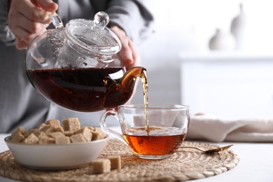 Photo of Woman pouring hot black tea into cup at white table, closeup