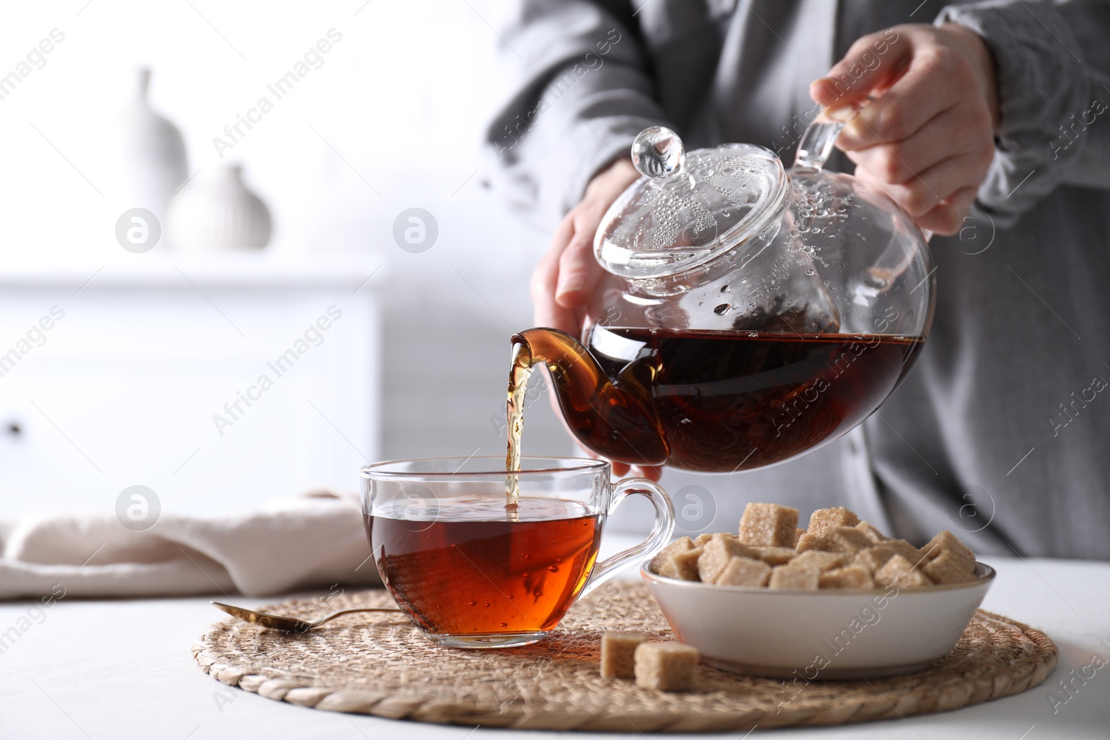 Photo of Woman pouring hot black tea into cup at white table, closeup