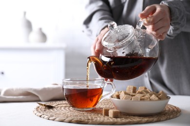 Photo of Woman pouring hot black tea into cup at white table, closeup