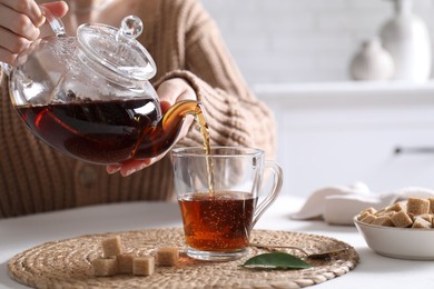 Photo of Woman pouring hot black tea into cup at white table, closeup