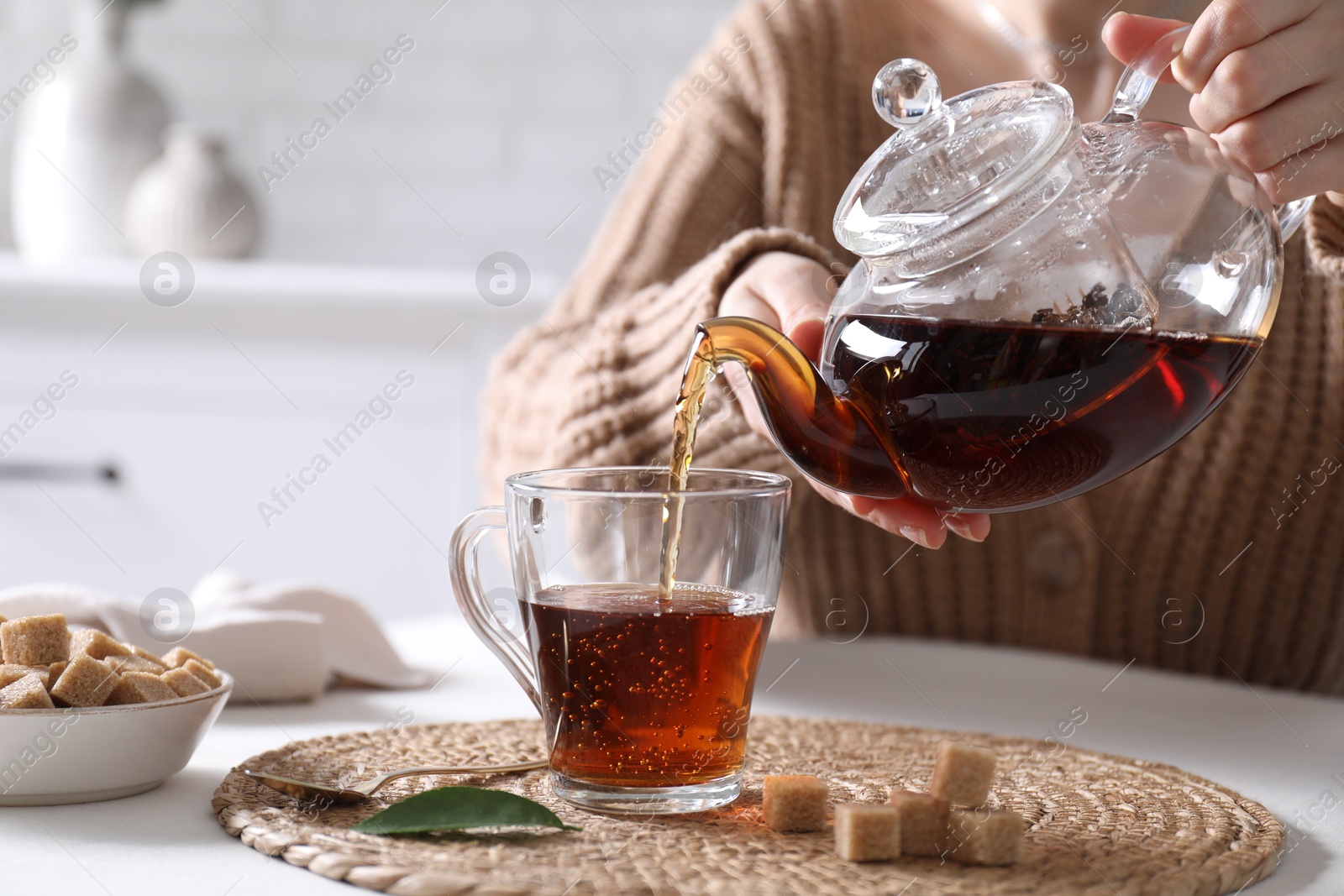 Photo of Woman pouring hot black tea into cup at white table, closeup