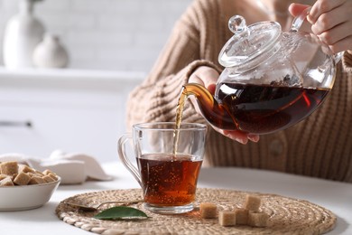 Photo of Woman pouring hot black tea into cup at white table, closeup