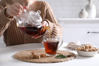 Photo of Woman pouring hot black tea into cup at white table, closeup