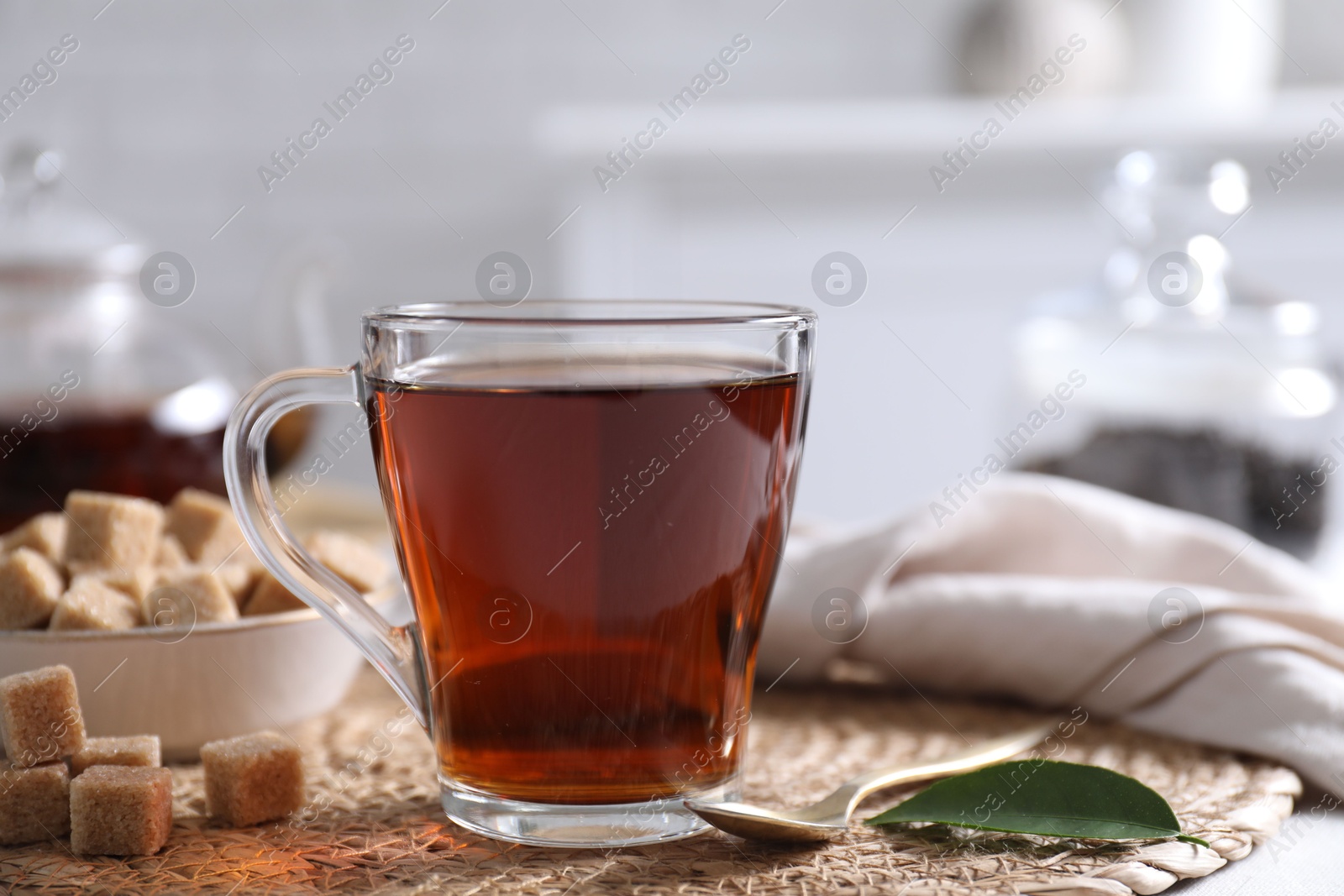 Photo of Aromatic black tea in cup and brown sugar cubes on table, closeup