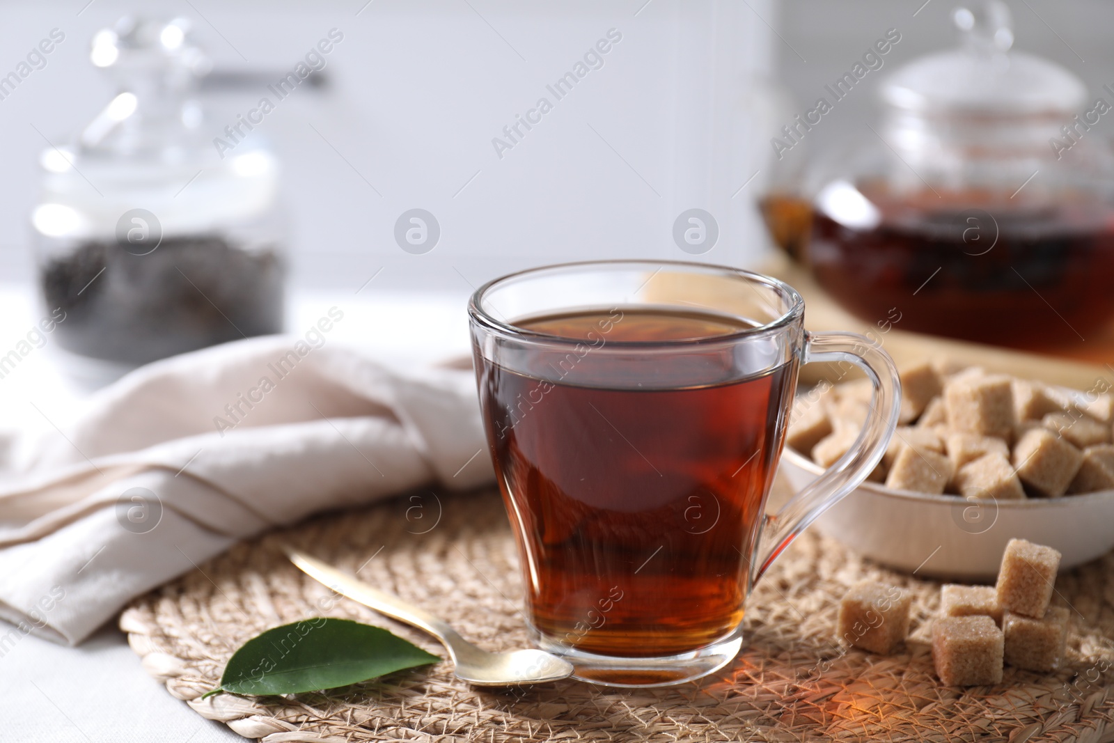 Photo of Aromatic black tea in cup and brown sugar cubes on table, closeup