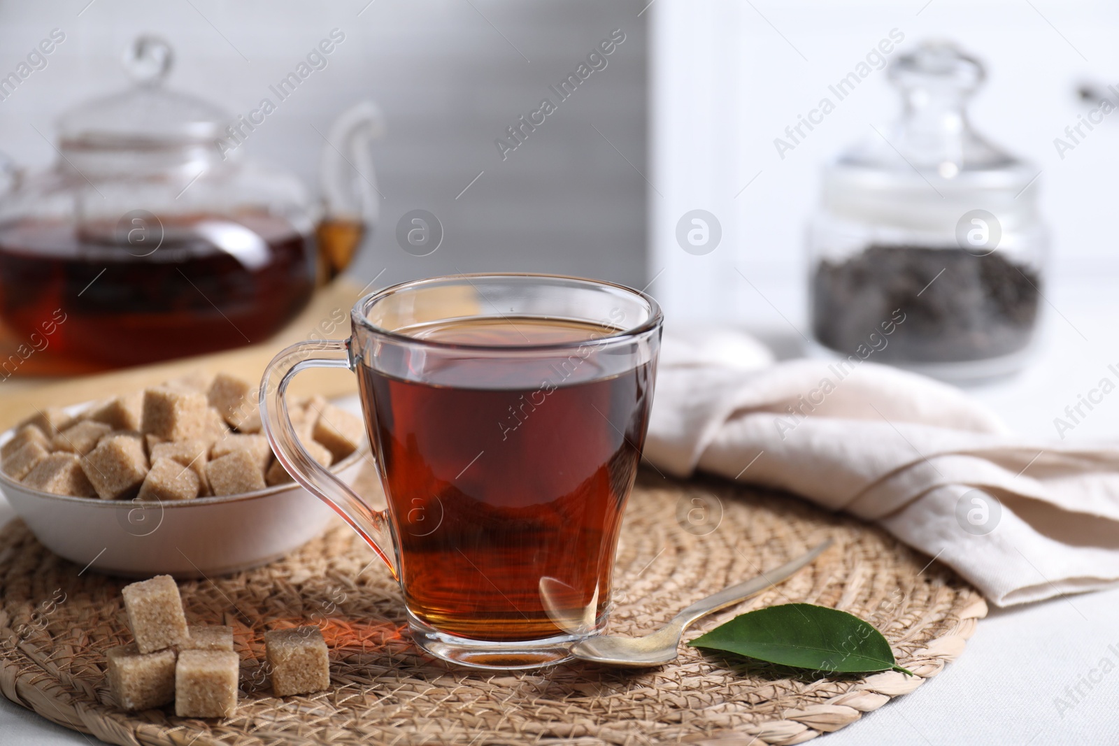 Photo of Aromatic black tea in cup and brown sugar cubes on white table, closeup