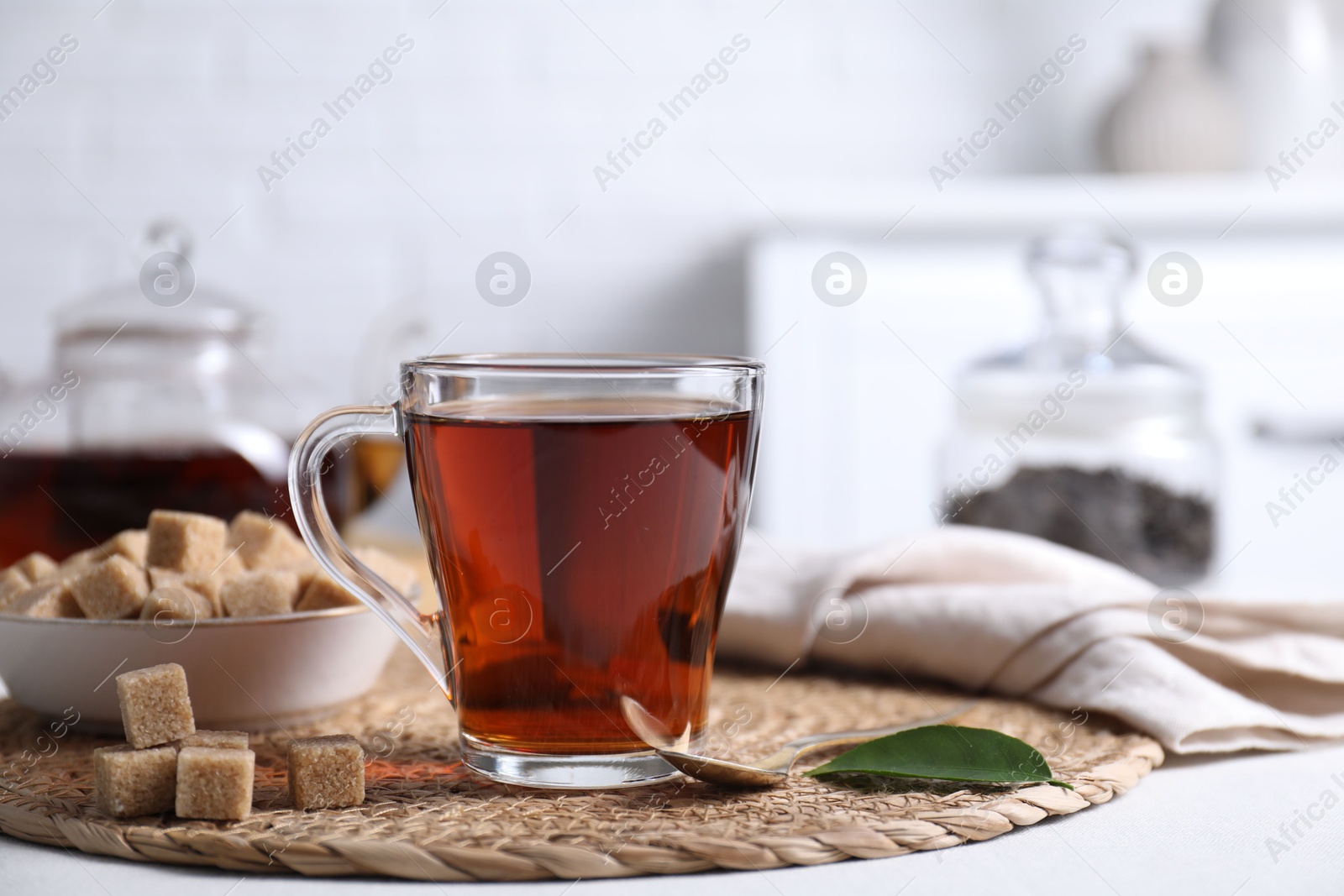 Photo of Aromatic black tea in cup and brown sugar cubes on white table