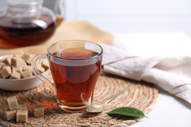 Photo of Aromatic black tea in cup and brown sugar cubes on white table, closeup. Space for text