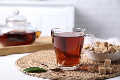 Photo of Aromatic black tea in cup and brown sugar cubes on white table, closeup