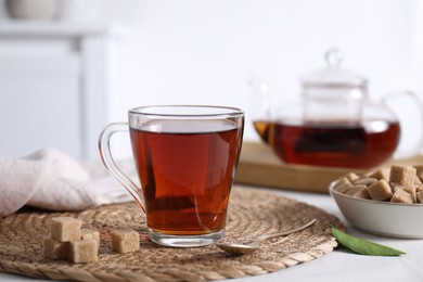 Photo of Aromatic black tea in cup and brown sugar cubes on white table, closeup