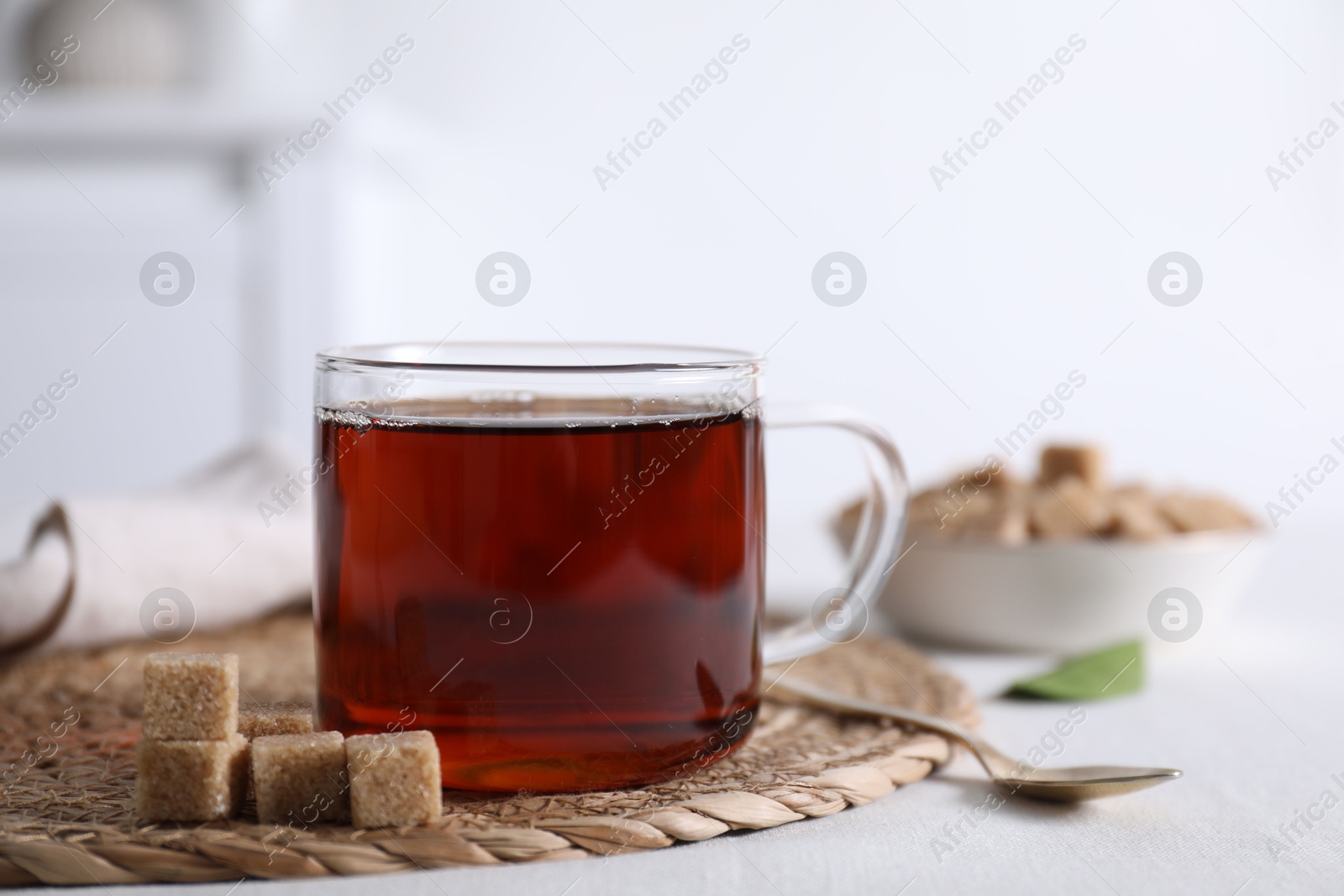 Photo of Aromatic black tea in cup and brown sugar cubes on white table, closeup