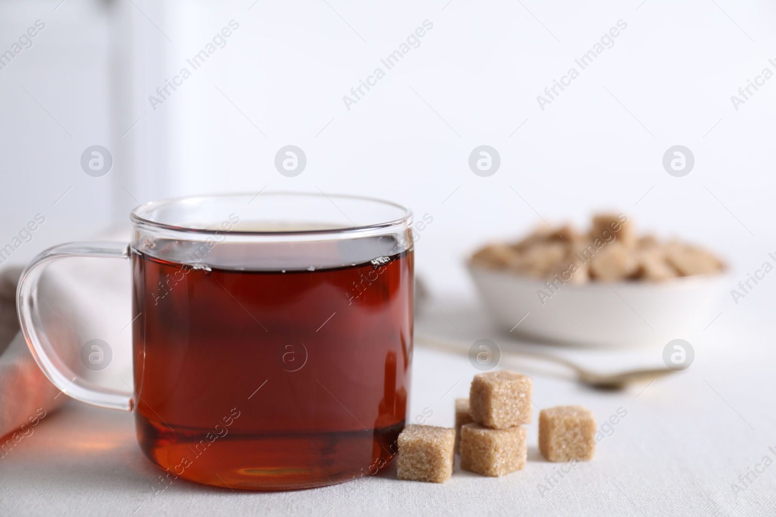 Photo of Aromatic black tea in cup and brown sugar cubes on white table, closeup