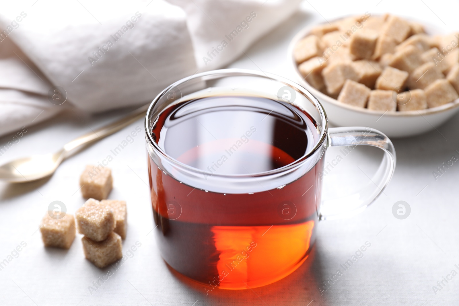 Photo of Aromatic black tea in cup and brown sugar cubes on white table, closeup