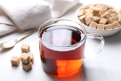 Photo of Aromatic black tea in cup and brown sugar cubes on white table, closeup