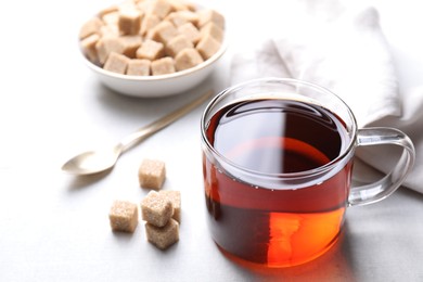 Photo of Aromatic black tea in cup and brown sugar cubes on white table, closeup