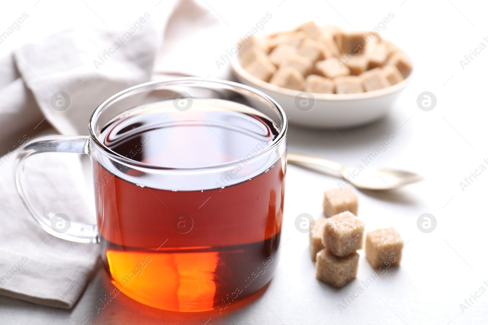 Photo of Aromatic black tea in cup and brown sugar cubes on white table, closeup