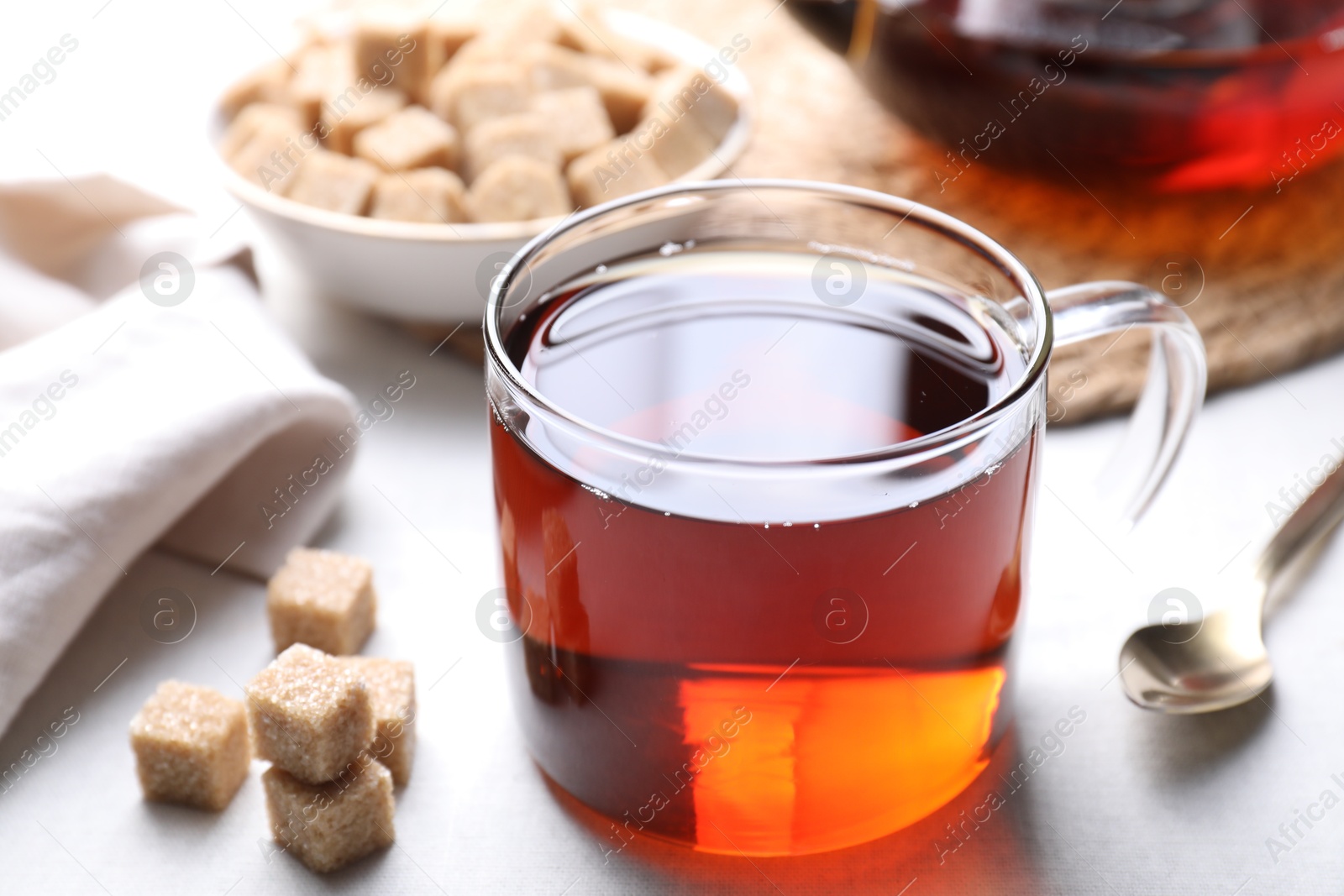 Photo of Aromatic black tea in cup and brown sugar cubes on white table, closeup