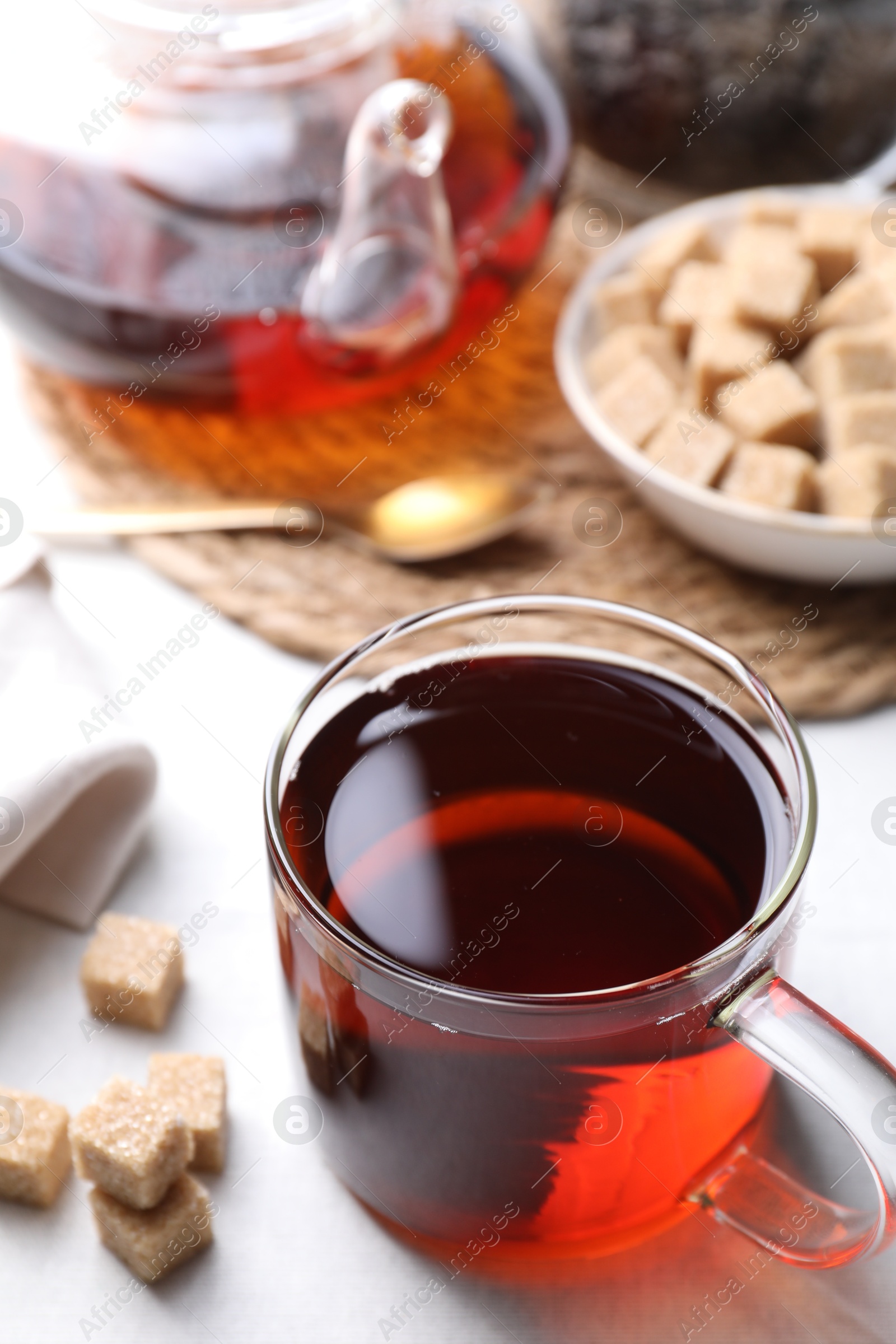 Photo of Aromatic black tea and brown sugar cubes on white table, closeup