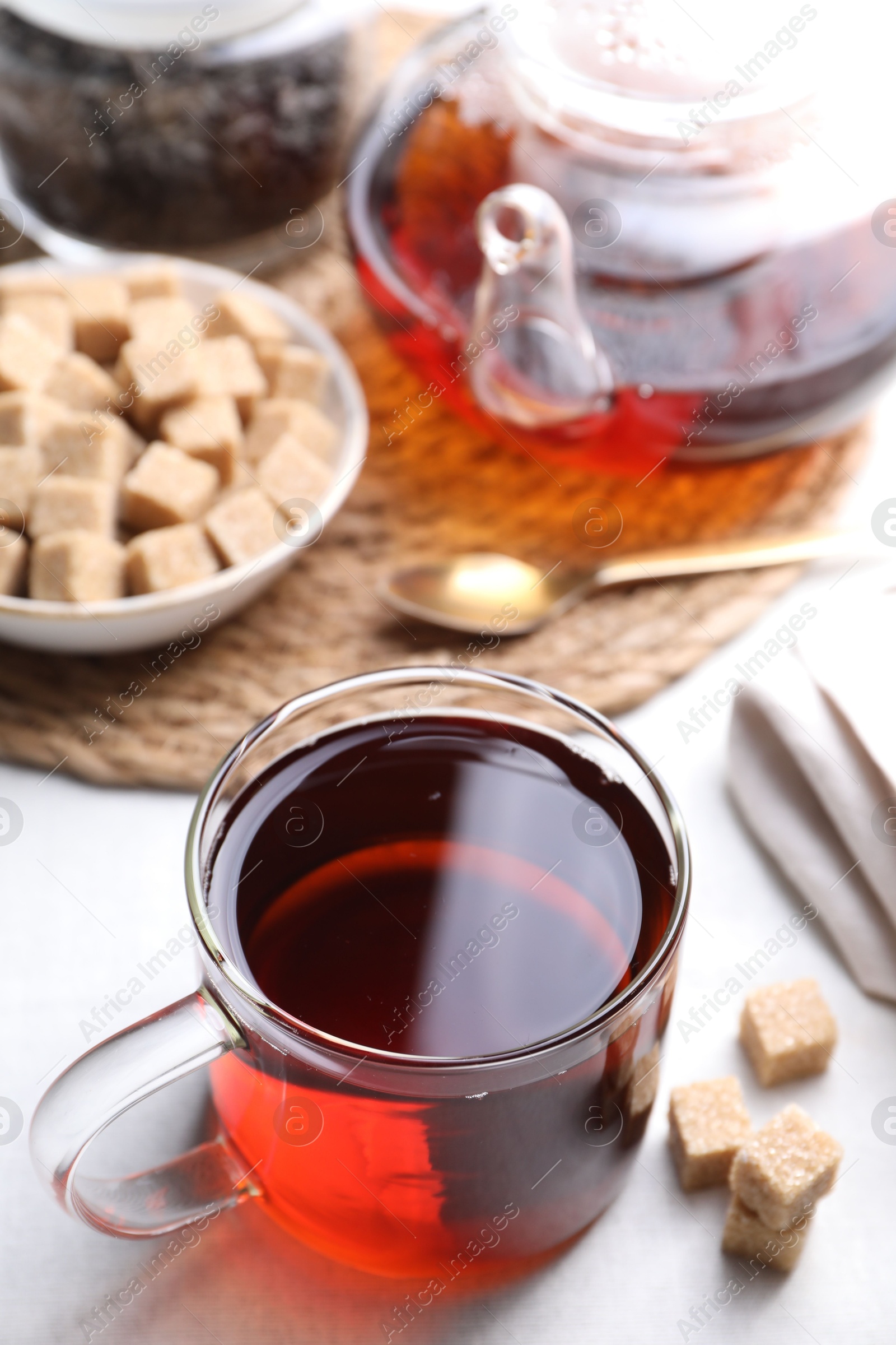 Photo of Aromatic black tea and brown sugar cubes on white table, closeup