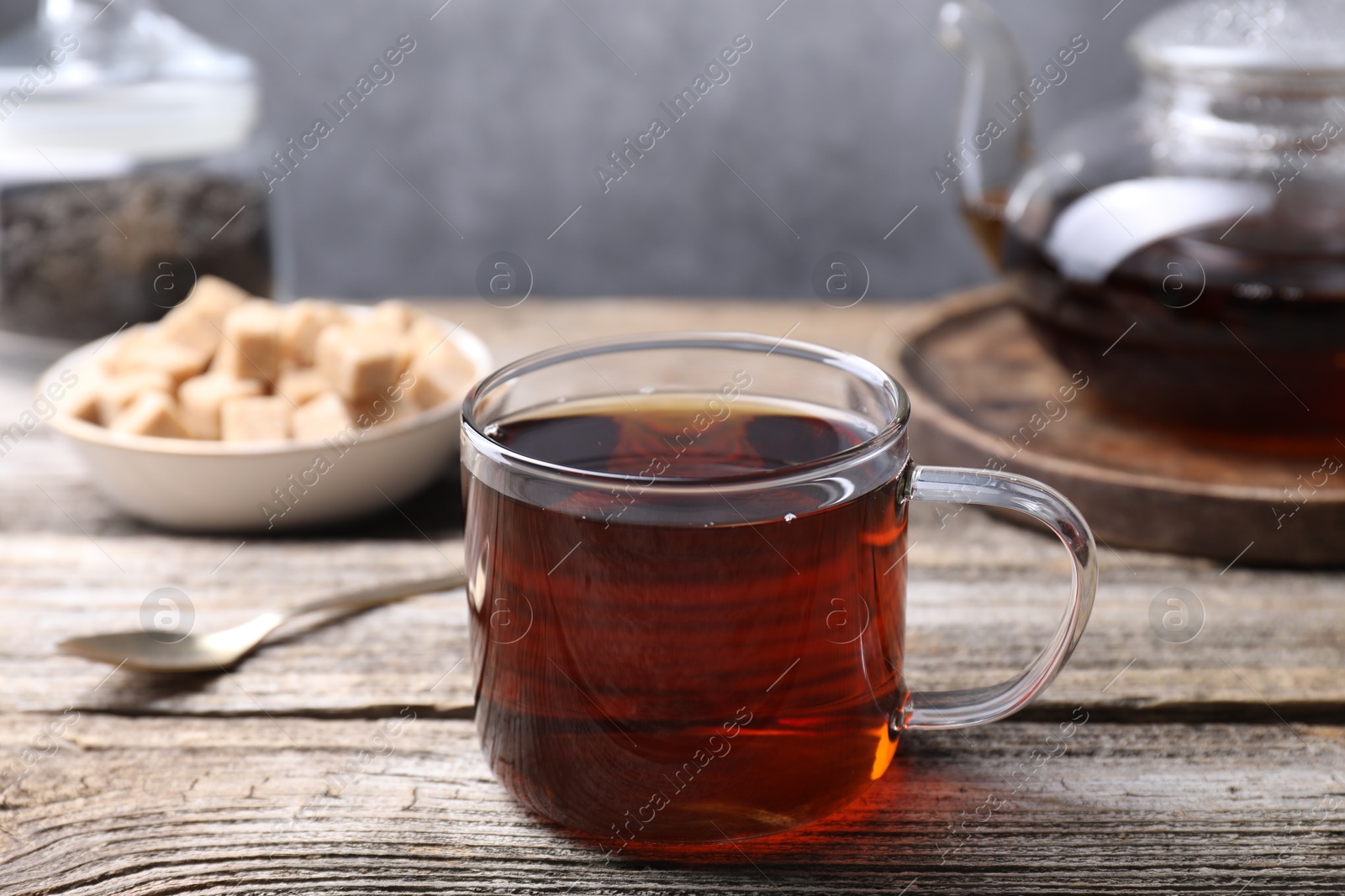 Photo of Aromatic black tea in cup and spoon on wooden table, closeup