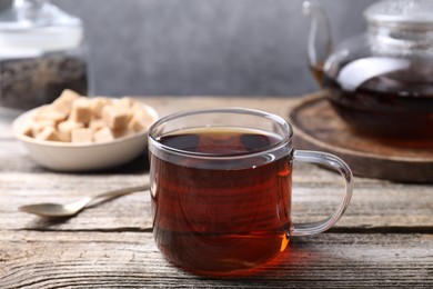 Photo of Aromatic black tea in cup and spoon on wooden table, closeup