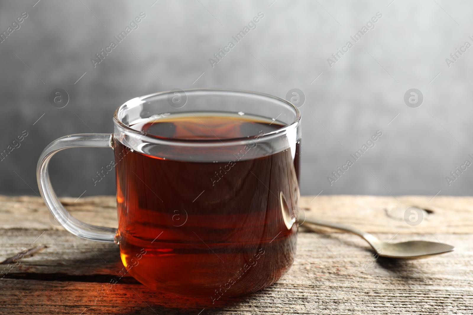 Photo of Aromatic black tea in cup and spoon on wooden table, closeup