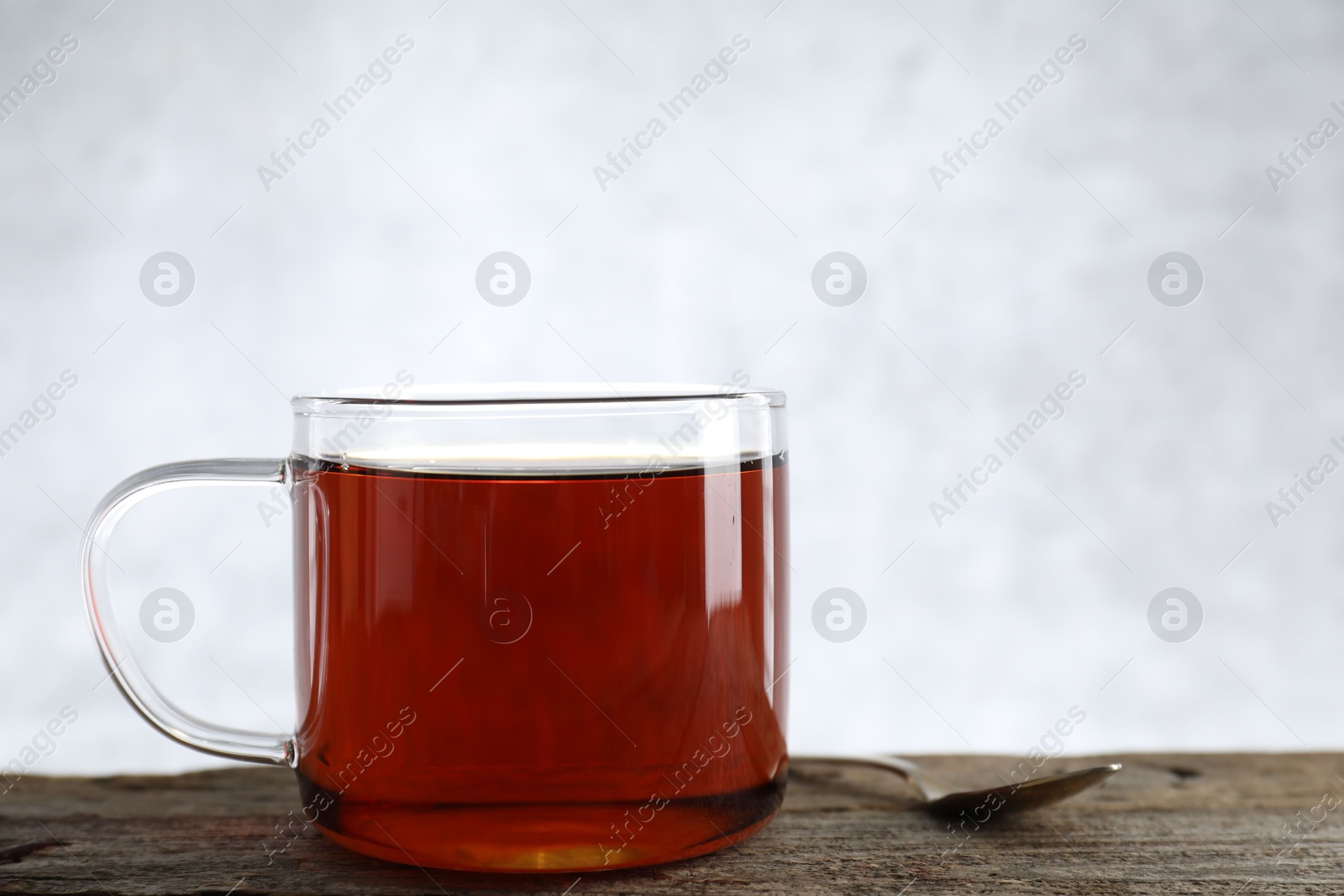 Photo of Aromatic black tea in cup and spoon on wooden table, closeup. Space for text