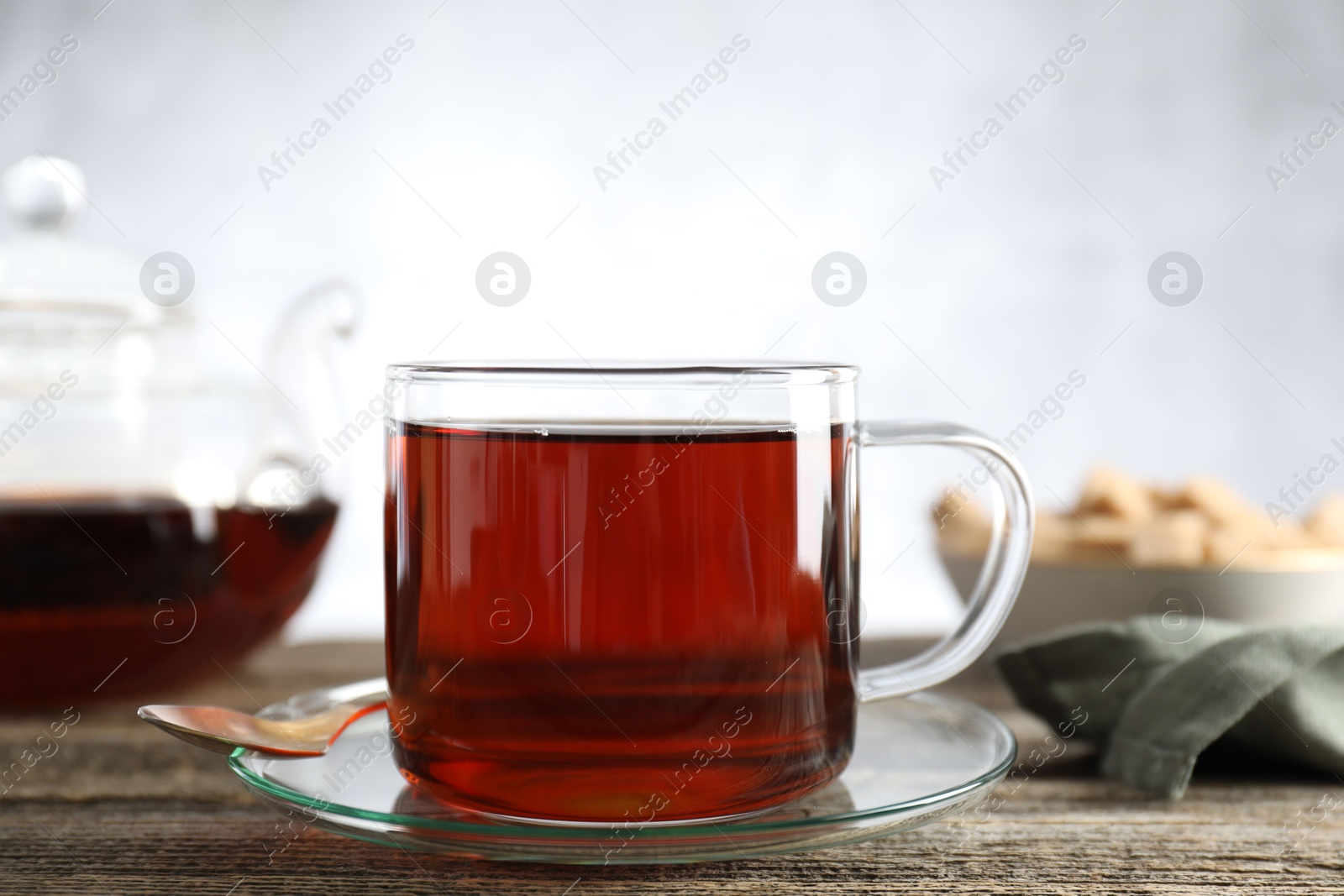 Photo of Aromatic black tea in cup and spoon on wooden table, closeup