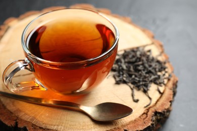 Photo of Aromatic black tea in cup and dry leaves on grey table, closeup