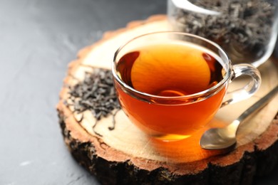 Photo of Aromatic black tea in cup and dry leaves on grey table, closeup