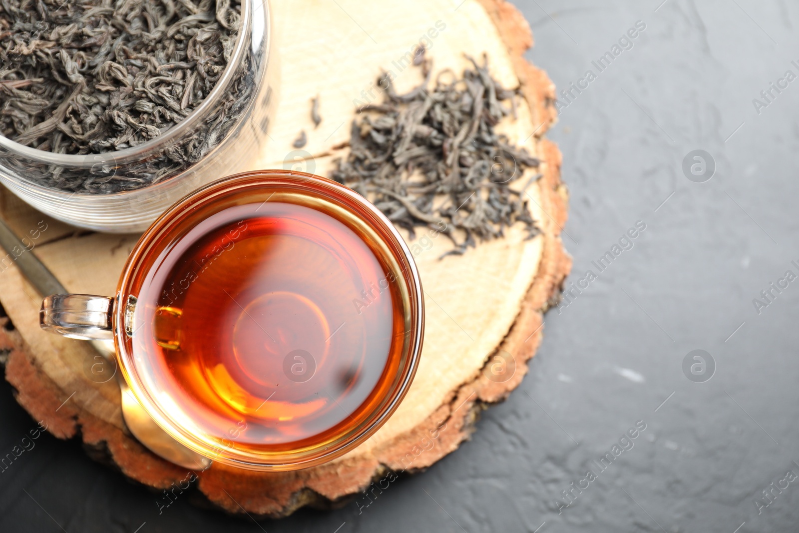 Photo of Aromatic black tea in cup and dry leaves on grey table, top view. Space for text